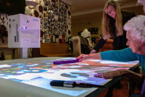 Image shows projector on wheels reflecting onto a table where older people use it to play a game