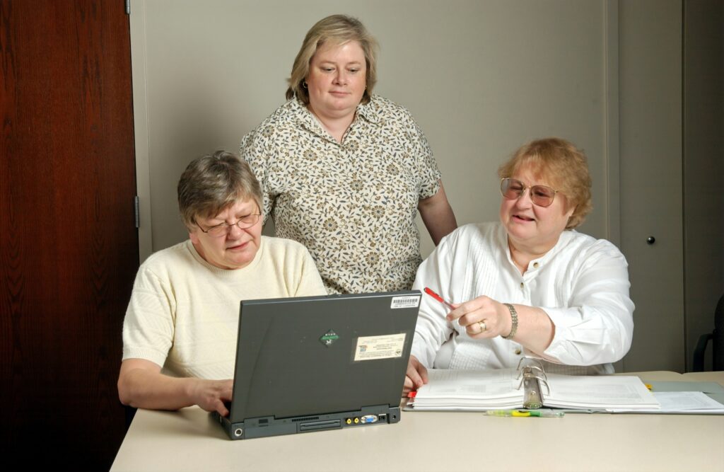 Three people gather together around a laptop, looking like they are adding information to the computer