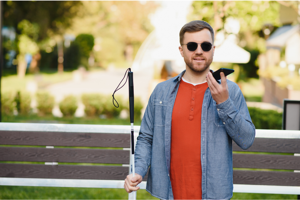 Man with sight impairment, outdoors with white stick and speaking into mobile phone